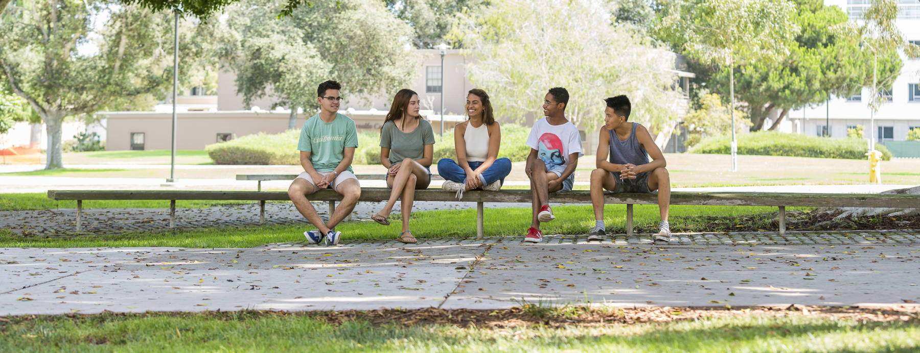 5 students sitting on a bench on a sunny day on UCSB's campus