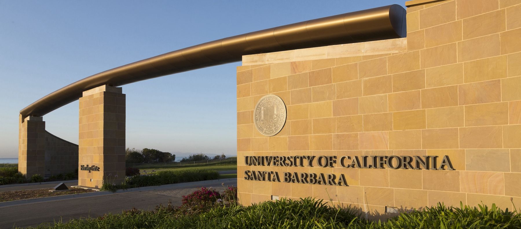 Henley Gate, a sand colored stone entry way, shines in the golden hour sunlight on UCSB's campus. 